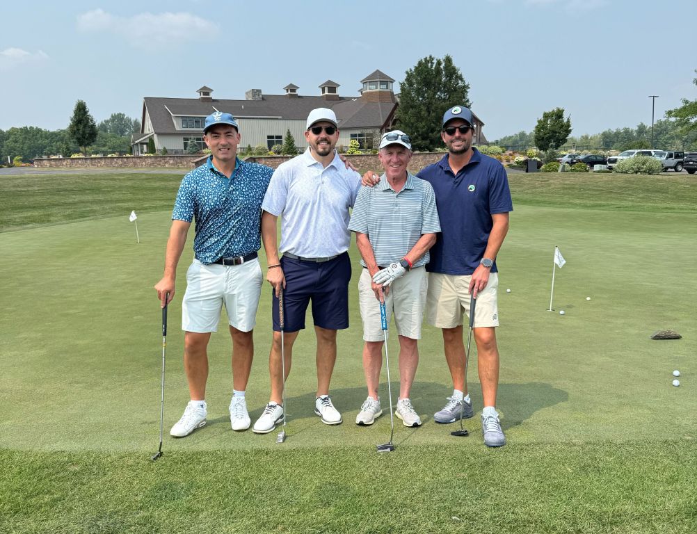 Mac Cummings and three fellow golfers stand on a putting green at a Cause for the Cuse Golf Tournament