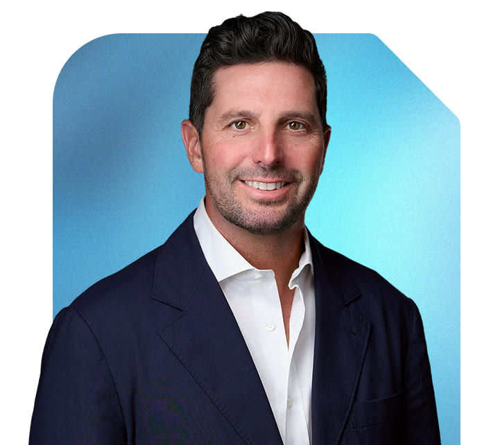 Mac Cummings, CEO and Cofounder of Terakeet, smiles in a blue suit and white button-down shirt